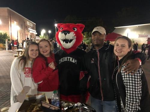 Four people stand with Pouncer at an evening alumni event